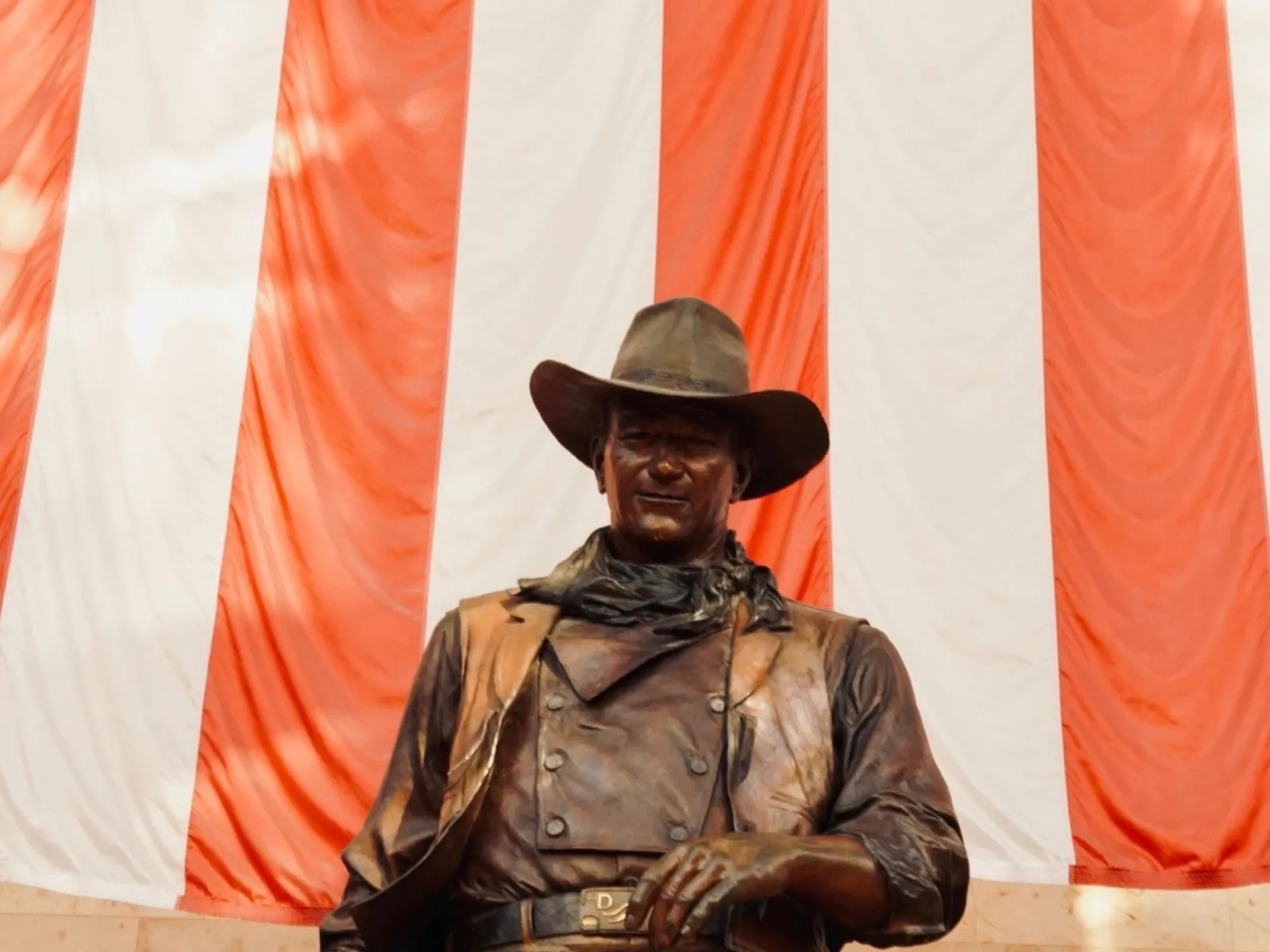 The John Wayne statue at John Wayne Airport, in front of a draped American flag